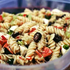 Ausgefallene Salate zum Grillen schnell gemacht: Nudelsalat mit Spiralnudeln, Oliven, Paprika und Brokkoli in einer Plastikschüssel.