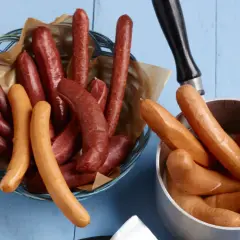 Bockwurst vs Bratwurst: Eine Auswahl an Würsten, einige dunkelrot in einem Korb, andere hellbraun in einem Topf.