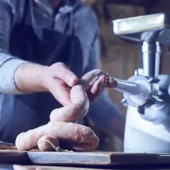 Mann stellt mit einer Wurstmaschine frische Würste her.