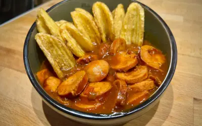 Eine Schüssel mit geschnittener Currywurst in Sauce und Kartoffelspalten. Perfekt für einen gemütlichen Abend, wie aus dem Dutch Oven.