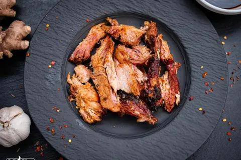 Zartes Pulled Pork auf schwarzem Teller, perfekt gegart. Die Kerntemperatur ist entscheidend für saftiges Fleisch. Ingwer und Knoblauch deuten auf würzige Aromen hin.