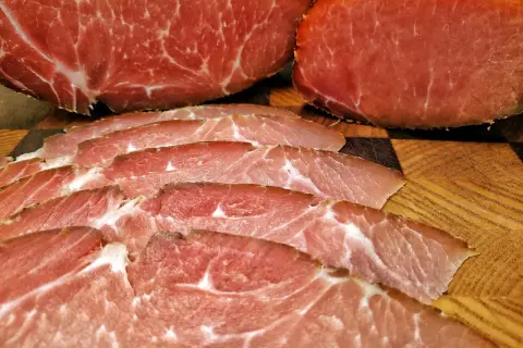 Dünn geschnittener Lachsschinken, der aus magerem Schweinefleisch besteht, liegt auf einem Holzbrett.