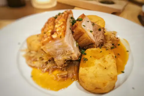 Saftiger Schweinebraten Niedrigtemperatur mit knuspriger Kruste, Kartoffelklößen und dunkler Soße auf einem weißen Teller.