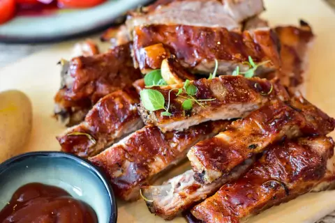 Saftige spareribs im backofen umluft: wie lange sie perfekt garen, zeigt dieses Bild. Dazu gibt es BBQ-Sauce und Kartoffeln.