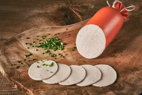 Eine angeschnittene Gelbwurst mit Schnittlauch bestreuten Scheiben auf einem Holzbrett.