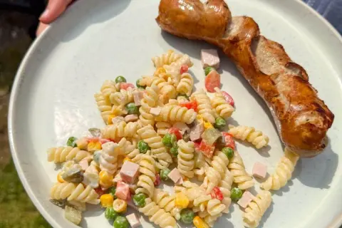 Ein herzhafter Nudelsalat mit Erbsen, Mais und Schinken, dazu eine goldbraune Bratwurst – perfekt, was passt zu Nudelsalat!