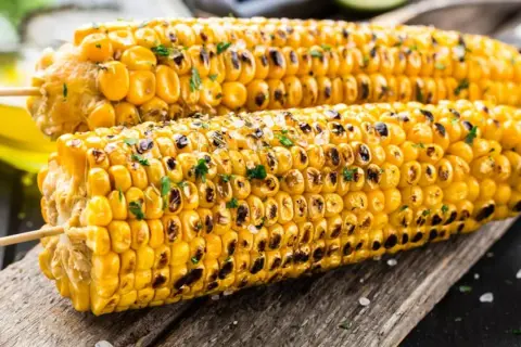 Zwei perfekt gegrillte Maiskolben mit gerösteten Stellen und Kräutern, bereit zum Genießen. Das Maiskolben grillen ist ein Sommergenuss.