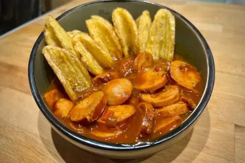 Eine Schüssel mit geschnittener Currywurst in Sauce und Kartoffelspalten. Perfekt für einen gemütlichen Abend, wie aus dem Dutch Oven.