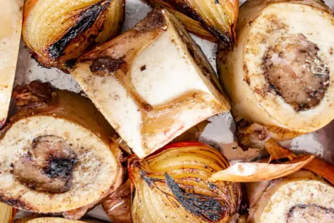 Geröstete Suppenknochen und Zwiebeln, bereit zum Kochen für eine herzhafte Brühe.
