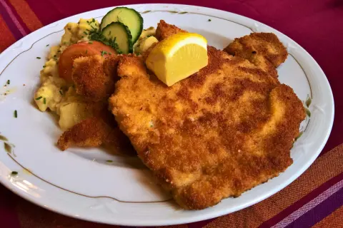 Perfekt paniertes Wiener Schnitzel mit Kartoffelsalat, Tomate, Gurke und Zitrone. Ein Genuss, der zeigt, wie gut Wiener Schnitzel panieren gelingt.