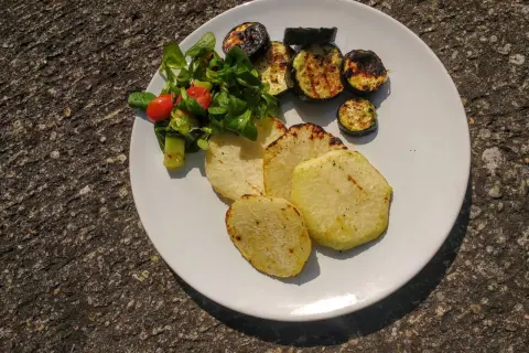 Gegrillte Kohlrabi-Scheiben mit Zucchini und einem kleinen Salat auf einem weißen Teller. Ein leckeres Sommergericht!