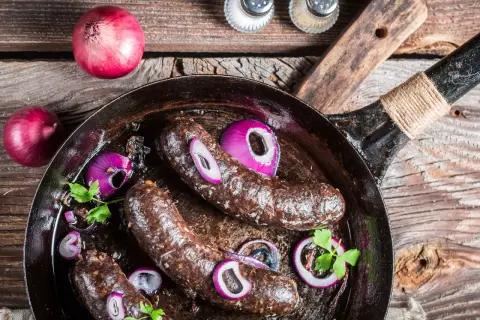 Bratwürste in der Pfanne mit Zwiebeln und Petersilie. Was ist Black Pudding? Eine herzhafte Wurstspezialität, die hier gebraten wird.