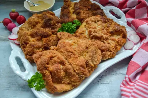 Goldbraun paniertes Schnitzel, perfekt zum Schnitzel panieren. Dazu Radieschen, Petersilie und Senf.