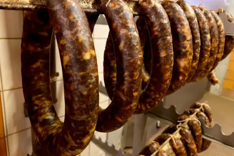 Reife, dunkle Würste hängen an einer Stange. Sie sehen aus wie eine traditionelle Chorizo, die zum Trocknen bereit ist.