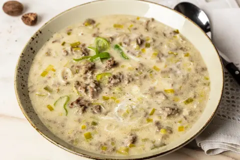 Eine cremige hackfleisch lauch suppe, garniert mit frischem Lauch und Gewürzen, serviert in einer rustikalen Schüssel.