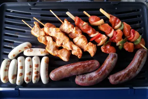Fleisch auf Gasgrill richtig grillen: Hähnchenspieße und Würstchen brutzeln auf dem Grill.