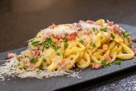 Ein Teller cremiger Spaghetti Carbonara, garniert mit Speckwürfeln, Petersilie und frisch geriebenem Parmesan.