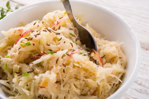 Schüssel mit Sauerkraut, verfeinert mit Kümmel und Apfelstücken. Eine Gabel ragt hinein, bereit zum Genießen.