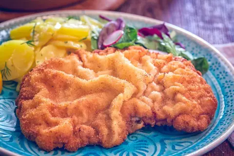 Goldbraunes Wiener Schnitzel mit Kartoffelsalat und frischem Grün. Ein perfektes Wiener Schnitzel Rezept für Genießer.