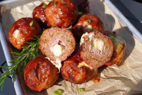 Leckere "Moink Balls" mit geschmolzenem Käse und Schinken im Inneren, glasiert und auf einem Blech mit Rosmarin garniert.