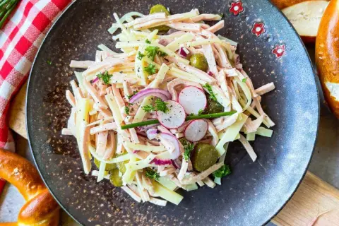 Ein herzhafter schweizer wurstsalat mit Käse, Radieschen, Gurken und Zwiebeln, garniert mit Petersilie.