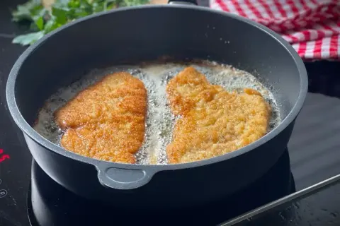 Zwei panierte Schnitzel braten in heißem Öl. Die goldbraune Kruste verspricht ein perfektes Ergebnis.