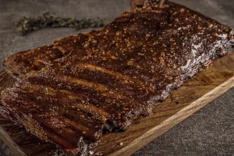Saftige Rippchen vom Wildschwein, mariniert und perfekt gegrillt, liegen auf einem Holzbrett. Ein Genuss für jeden Grillmeister!