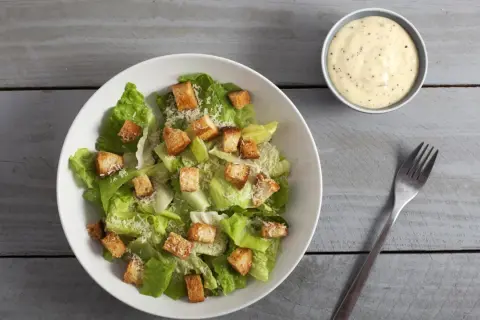 Frischer Caesar Salat mit knusprigen Croutons und Parmesan, dazu ein Schälchen cremiges Dressing.