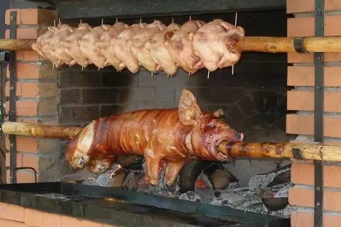 Ein Spanferkel grillen über offenem Feuer. Darüber hängen mehrere Hähnchen am Spieß.