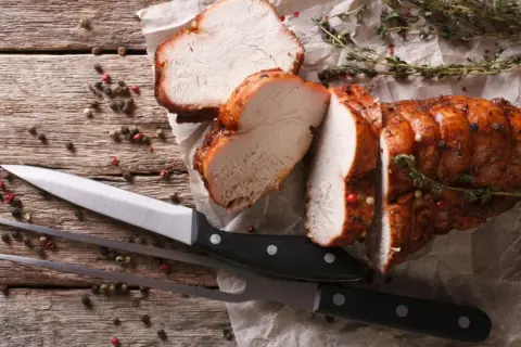Saftiges braten fleisch, aufgeschnitten, mit Kräutern und Pfefferkörnern auf Holz. Messer und Fleischgabel liegen bereit.