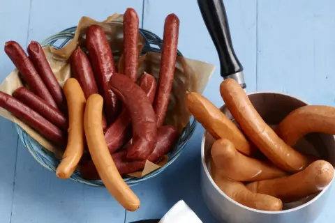 Bockwurst vs Bratwurst: Eine Auswahl an Würsten, einige dunkelrot in einem Korb, andere hellbraun in einem Topf.