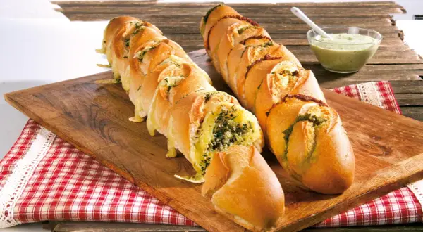 Zwei gefüllte Baguettes zum Grillen, eines mit Kräutern und Käse, das andere mit Pesto und Tomaten, daneben eine Schüssel Dip.