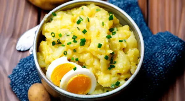 Schüssel mit warmem Kartoffelsalat, garniert mit Schnittlauch und Ei. Ein Klassiker, der immer schmeckt.
