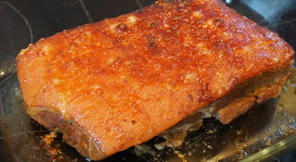 Saftiger Schweinebraten sous vide mit knuspriger Kruste, glänzend und goldbraun, ruht in einer Glasschale.