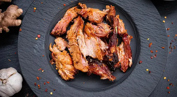 Zartes Pulled Pork auf schwarzem Teller, perfekt gegart. Die Kerntemperatur ist entscheidend für saftiges Fleisch. Ingwer und Knoblauch deuten auf würzige Aromen hin.