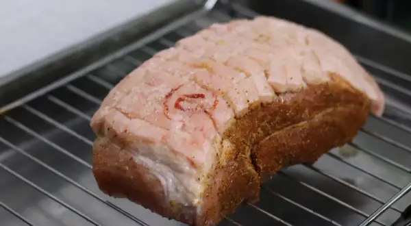 Ein Krustenbraten liegt auf einem Rost, bereit zum Krustenbraten grillen. Die Schwarte ist eingeschnitten und mit Gewürzen bestreut.