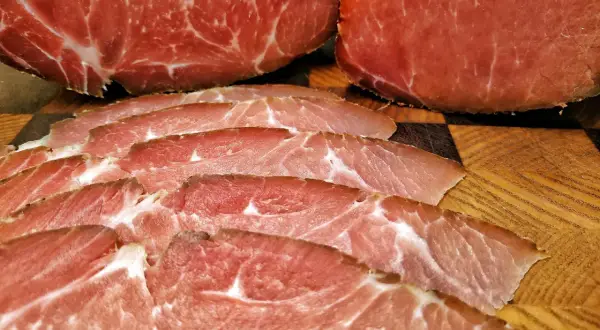Dünn geschnittener Lachsschinken, der aus magerem Schweinefleisch besteht, liegt auf einem Holzbrett.