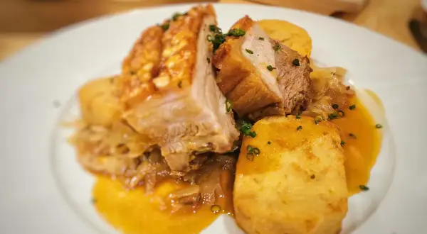 Saftiger Schweinebraten Niedrigtemperatur mit knuspriger Kruste, Kartoffelklößen und dunkler Soße auf einem weißen Teller.