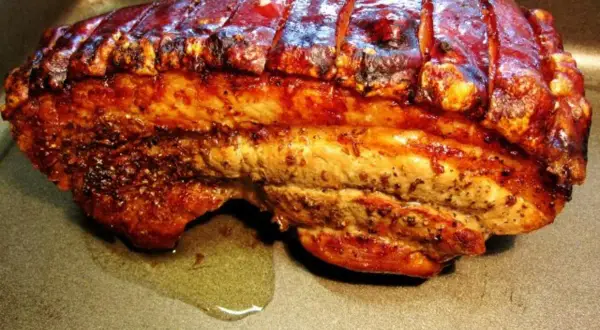 Perfekt gegrillter Schweinebauch mit knuspriger Schwarte liegt in einer Bratpfanne. Der Bratensaft glänzt daneben.