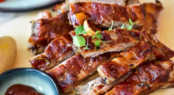 Saftige spareribs im backofen umluft: wie lange sie perfekt garen, zeigt dieses Bild. Dazu gibt es BBQ-Sauce und Kartoffeln.
