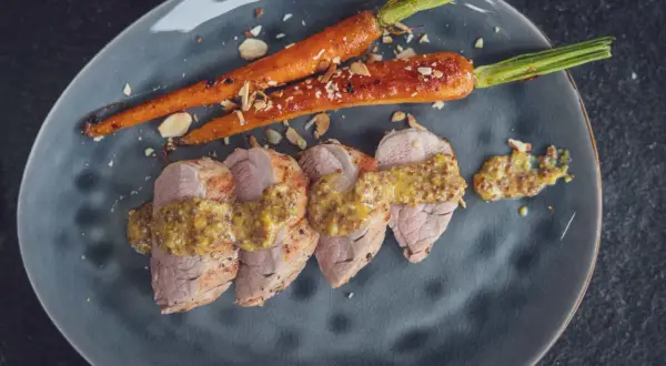 Zarte Scheiben von **schweinefilet grillen** mit Honig-Senf-Sauce und karamellisierten Karotten, bestreut mit Mandelsplittern.