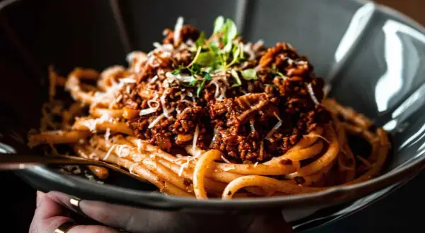 Eine Schüssel mit köstlichen Spaghetti Bolognese, garniert mit frischen Kräutern und geriebenem Parmesan.