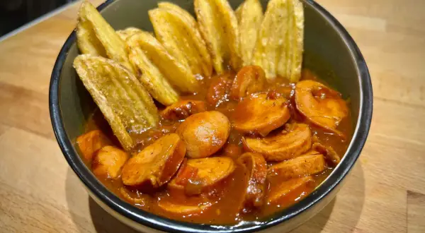 Eine Schüssel mit geschnittener Currywurst in Sauce und Kartoffelspalten. Perfekt für einen gemütlichen Abend, wie aus dem Dutch Oven.