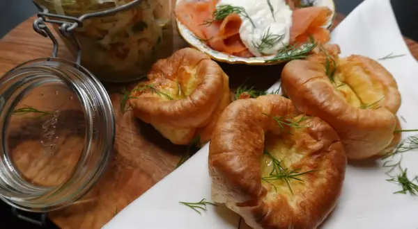 Goldbraune Yorkshire Pudding-Törtchen mit Dill garniert, daneben Lachs mit Frischkäse und ein Glas Sauerkraut.