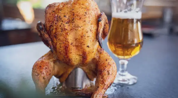 Ein goldbraunes Bierdosenhähnchen, saftig und gewürzt, steht neben einem Glas Bier.