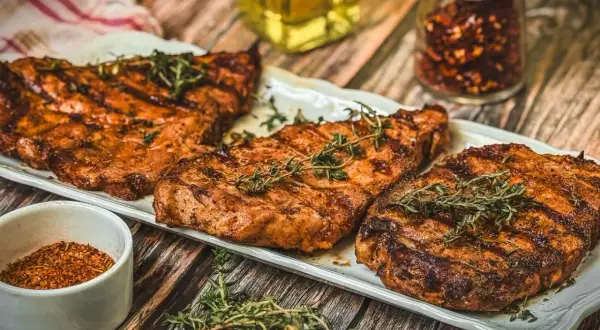 Saftige Nackensteaks vom Grill, garniert mit frischem Thymian. Daneben eine Schale Gewürzmischung und ein Glas Chiliflocken.