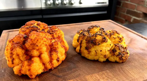 Zwei perfekt gegrillte Blumenkohlröschen liegen auf einem Holzbrett. Sie sind goldbraun und leicht angekohlt, was auf köstliches blumenkohl grillen hindeutet.