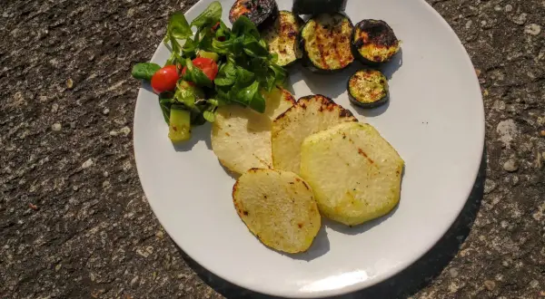 Gegrillte Kohlrabi-Scheiben mit Zucchini und einem kleinen Salat auf einem weißen Teller. Ein leckeres Sommergericht!