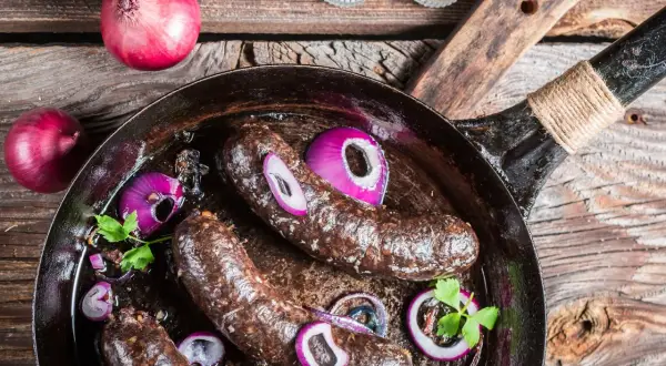 Bratwürste in der Pfanne mit Zwiebeln und Petersilie. Was ist Black Pudding? Eine herzhafte Wurstspezialität, die hier gebraten wird.