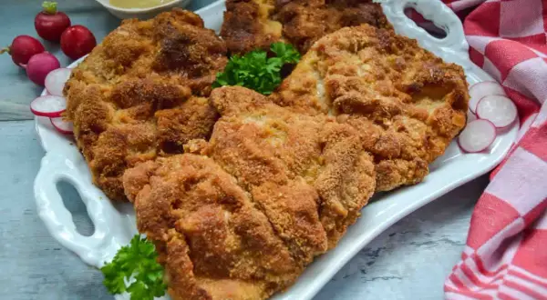 Goldbraun paniertes Schnitzel, perfekt zum Schnitzel panieren. Dazu Radieschen, Petersilie und Senf.